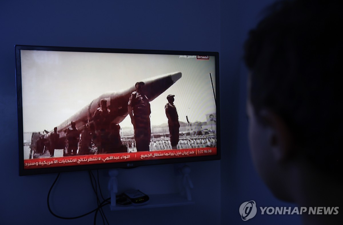 예멘 사나의 한 시민이 미사일 옆에 도열한 후티 반군 전투원들이 나오는 TV 화면을 보는 모습